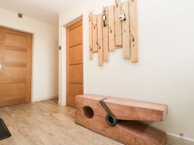 A hallway with wooden doors a wooden bench shaped like a clothespin and a wall-mounted wooden coat rack at Palace Bungalow in St Weonards