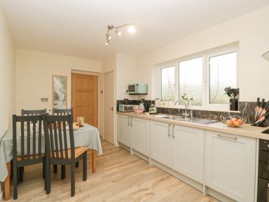 A kitchen with a dining table and chairs next to cupboards and a window at Palace Bungalow in St Weonards
