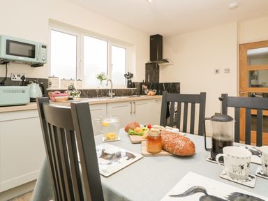 A kitchen with black chairs around a table set with bread and drinks at Palace Bungalow in St Weonards