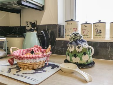 A kitchen counter with a kettle tea cozy baskets and labeled containers at Palace Bungalow in St Weonards