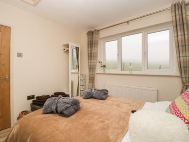 A bedroom with a bed a large window a mirror and folded robes at Palace Bungalow in St Weonards