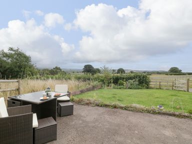 An outdoor patio with a table and chairs overlooking a grassy garden and a fenced field at Palace Bungalow in St Weonards