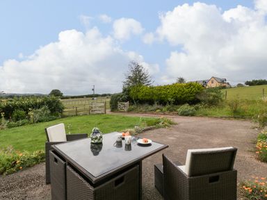 An outdoor patio with a table and two chairs overlooking a garden and fields at Palace Bungalow in St Weonards