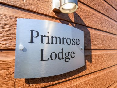 A metal sign with the words Primrose Lodge mounted on a wooden wall under a light at Primrose Lodge in Runswick Bay near Staithes
