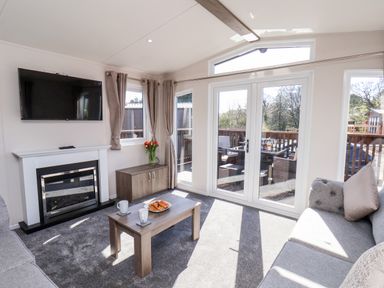 A living room with a wall-mounted TV fireplace sofa coffee table and glass doors leading to an outdoor seating area at Primrose Lodge in Runswick Bay near Staithes