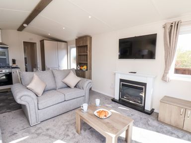A living room with a gray sofa coffee table with croissants mugs wall mounted tv and fireplace at Primrose Lodge in Runswick Bay near Staithes