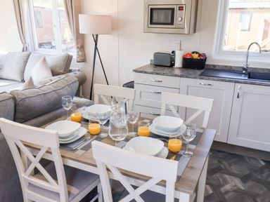 A dining table set for four with bowls glasses and orange juice next to a kitchen area with microwave toaster and sink at Primrose Lodge in Runswick Bay near Staithes