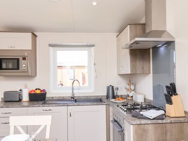 A kitchen with a sink under a window a gas stove with an oven a microwave a kettle a knife set and a toaster at Primrose Lodge in Runswick Bay near Staithes