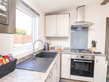 A kitchen with a sink under a window a gas stove oven and a knife block at Primrose Lodge in Runswick Bay near Staithes