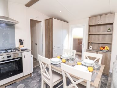 A dining area with a table set for four next to a kitchen with cabinets and a stove at Primrose Lodge in Runswick Bay near Staithes