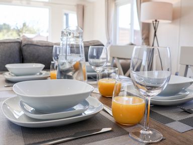 A dining table with white dishes glasses of orange juice and a pitcher in a room at Primrose Lodge in Runswick Bay near Staithes