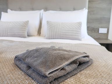 A folded gray towel on a bed with white pillows and gray cushions at Primrose Lodge in Runswick Bay near Staithes
