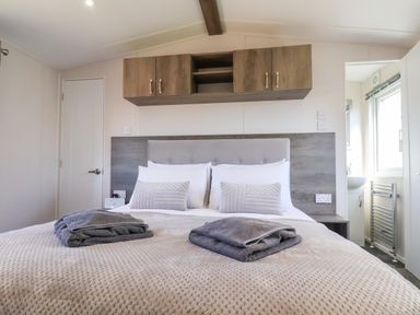 A bedroom with a bed with pillows and folded towels and overhead cabinets at Primrose Lodge in Runswick Bay near Staithes
