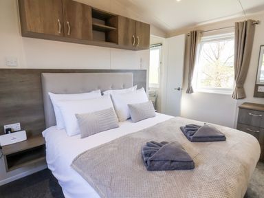 A bedroom with a double bed folded towels headboard overhead cabinets and two windows at Primrose Lodge in Runswick Bay near Staithes