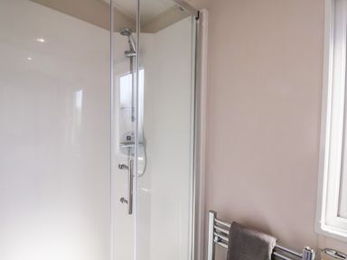 A shower enclosure with glass door and chrome handle and a towel on a chrome radiator at Primrose Lodge in Runswick Bay near Staithes