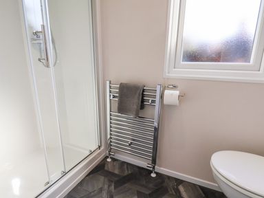 A bathroom with a shower enclosure a radiator with a gray towel a toilet and a frosted window at Primrose Lodge in Runswick Bay near Staithes
