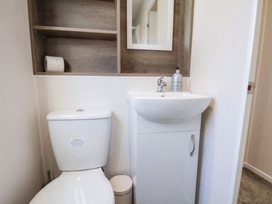 A small bathroom with a toilet sink a mirror and shelving at Primrose Lodge in Runswick Bay near Staithes