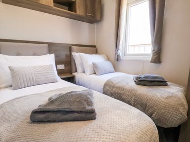 A bedroom with two single beds with grey blankets and pillows near a window at Primrose Lodge in Runswick Bay near Staithes