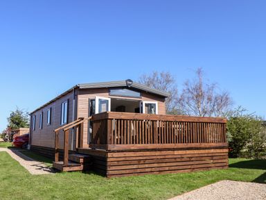A small wooden cabin with a porch and stairs on grass under a clear blue sky