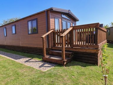 A wooden mobile home with a small deck and steps on grass with a gravel path nearby at Primrose Lodge in Runswick Bay near Staithes