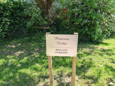 A sign reading Primrose Lodge private parking on a grassy area with shrubs and a tree in the background at Primrose Lodge in Runswick Bay near Staithes