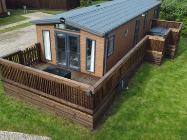 A wooden cabin with a fenced deck and hot tub on a grassy area at Primrose Lodge in Runswick Bay near Staithes