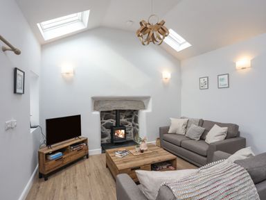 A sitting room with two grey sofas a wooden coffee table a wood burning stove and a TV at Tan Y Coed - Nasareth Nasareth near Penygroes