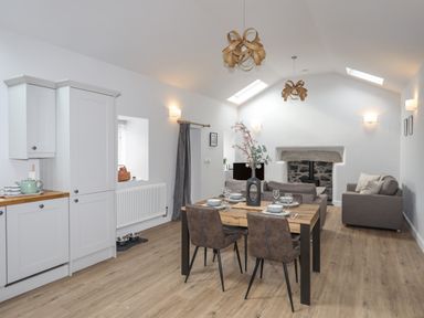 An open-plan kitchen and living area with a dining table set for four and a stone fireplace at Tan Y Coed - Nasareth Nasareth near Penygroes