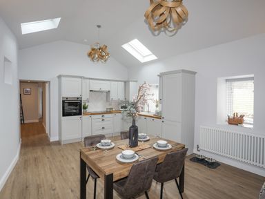 A kitchen and dining area with a wooden table set for four and white cabinets at Tan Y Coed - Nasareth Nasareth near Penygroes