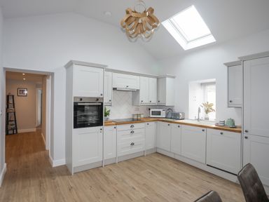 A kitchen with white cabinets wooden countertops a built in oven microwave and a skylight at Tan Y Coed - Nasareth in Nasareth near Penygroes