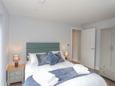 A bedroom with a bed with cushions and folded towels two bedside tables with lamps and a wardrobe at Tan Y Coed - Nasareth in Nasareth near Penygroes