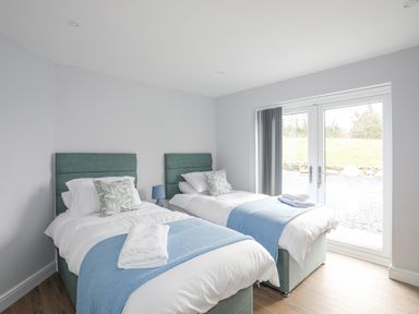 A bedroom with two single beds with blue throws and pillows next to glass doors at Tan Y Coed - Nasareth in Nasareth near Penygroes