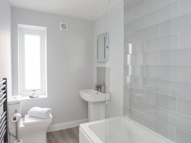 A bathroom with a toilet, sink, bathtub, window, and tiled wall at Tan Y Coed - Nasareth Nasareth near Penygroes