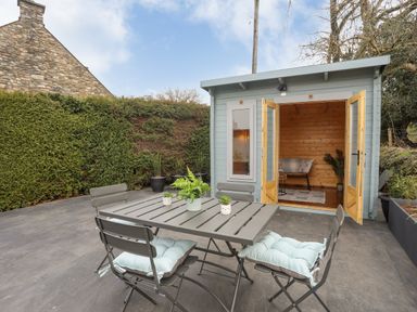 A patio with a metal table and chairs with cushions and plants on the table next to a small wooden shed with open doors at Tan Y Coed - Nasareth Nasareth near Penygroes