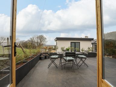 An outdoor patio with a table and chairs with plants in pots and raised planters at Tan Y Coed - Nasareth in Nasareth near Penygroes