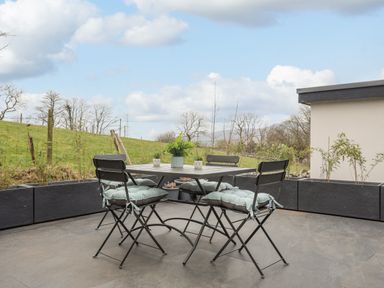 An outdoor patio with a table and four chairs with cushions and potted plants in a garden at Tan Y Coed - Nasareth in Nasareth near Penygroes