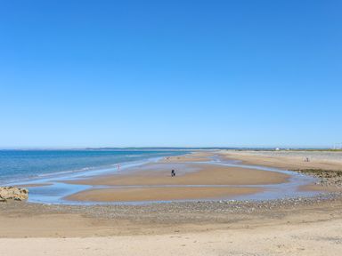 A sandy beach with people walking near the water and a clear blue sky at Tan Y Coed - Nasareth Nasareth near Penygroes