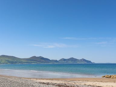A beach with sand and pebbles overlooking blue sea and mountains under a clear sky at Tan Y Coed - Nasareth Nasareth near Penygroes