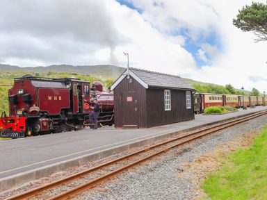A steam train stopped at a rural train station platform with a small wooden building on the platform at Tan Y Coed - Nasareth near Penygroes