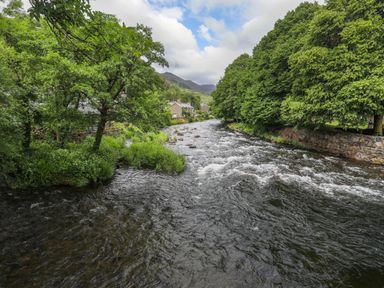A flowing river with trees and houses along the banks at Tan Y Coed - Nasareth in Nasareth near Penygroes