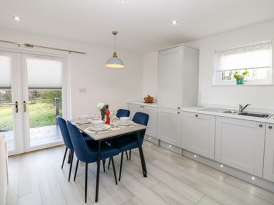 A kitchen dining area with a table set for four and blue chairs next to a cabinet and a sink at Harry's Lodge in Ashover