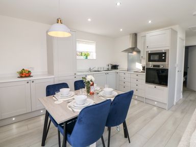 A kitchen with white cabinets a dining table set for four with blue chairs and built in oven at Harry's Lodge in Ashover