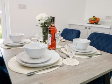 A dining table set with white bowls plates cutlery glasses a pink wine bottle and flowers at Harry's Lodge in Ashover