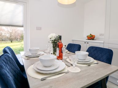 A dining table set with white dishes glasses a bottle of wine and flowers with blue chairs at Harry's Lodge in Ashover