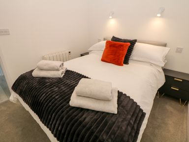 A bedroom with a bed with white sheets gray and orange pillows folded towels bedside tables with lamps at Harry's Lodge in Ashover