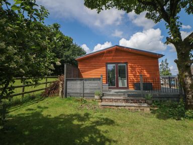 A wooden cabin with a small deck and glass doors surrounded by grass and trees at Harry's Lodge in Ashover