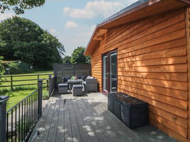 A wooden deck with outdoor furniture and a storage box next to a wooden building at Harry's Lodge in Ashover
