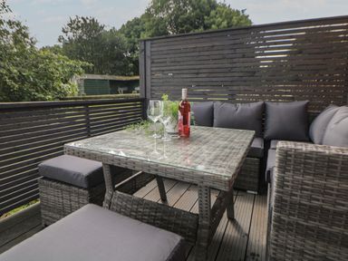 An outdoor seating area with a rattan table and cushioned seats with a bottle of wine and glasses at Harry's Lodge in Ashover