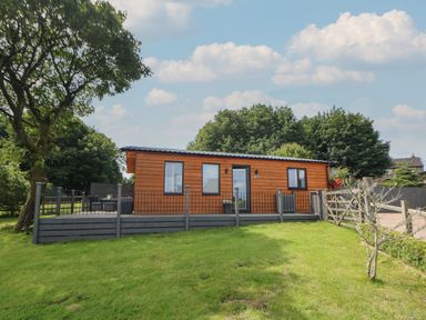 A wooden cabin with a deck and railing on a grassy lawn at Harry's Lodge in Ashover