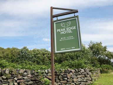 A sign for Peak Edge Hotel and Red Lion Restaurant near a stone wall with trees and grass